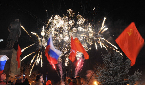 People wave Russian and Soviet flags as they look at fireworks in the center of the Crimean city of Sevastopol celebrating the annexation of the peninsula by Russia (Photo Credit: Viktor Drachev/AFP/Getty Images).