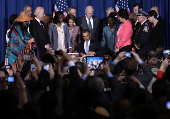 U.S. President Barack Obama (C), joined by (L-R) Vice Chairwoman of the Tulalip Tribes of Washington State Deborah Parker, Attorney General Eric Holder, Vice President Joseph Biden, trafficking survivor Tysheena Rhames, House Minority Leader Rep. Nancy Pelosi (D-CA), Sen. Michael Crapo (R-ID), Sen. Patrick Leahy (D-VT), House Minority Whip Rep. Steny Hoyer (D-MD), Rep. Gwen Moore (D-WI), Director of Public Policy of Casa de Esperanza Rosemary Hidalgo-McCabe, Rep. John Conyers (D-MI), Rep. Tom Cole (R-OK), Police Chief James Johnson of Baltimore County in Maryland, and Executive Director of New York City Anti-Violence Project Police Department Sharon Stapel, signs the Violence Against Women Act into law at the Department of the Interior March 7, 2013 in Washington, DC. The law expands protections for victims of domestic violence, sexual assault and trafficking.  (Photo by Alex Wong/Getty Images)