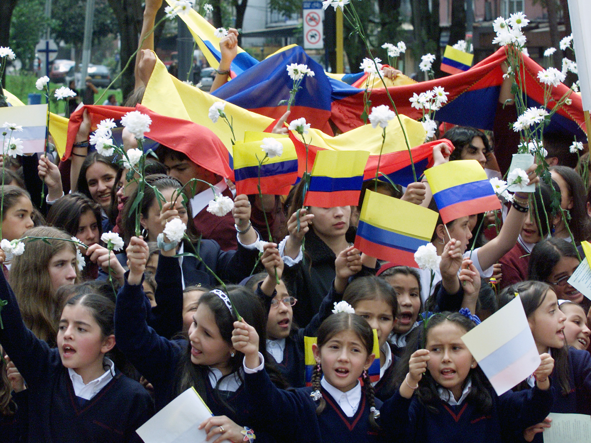 Students celebrating International Women's Day hold Colombian flags and flowers during march to demand the release of dozens of kidnapped children, Bogota.