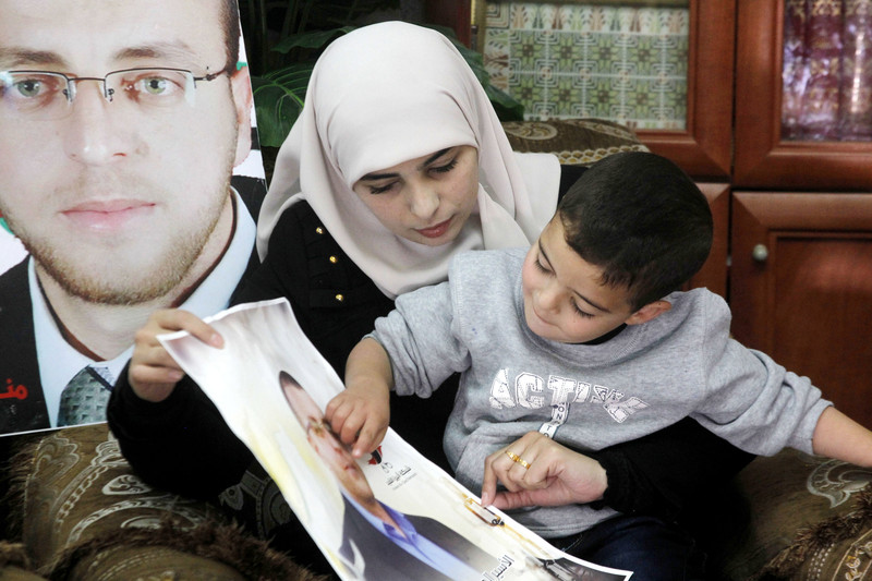Fayha Shalash, the wife of Palestinian journalist Muhammed al-Qiq, sits with her son at her home in the West Bank village of Dura on January 20, 2016. Al Qiq is seen in the poster.  Photo: Wisam Hashlamoun/APA images